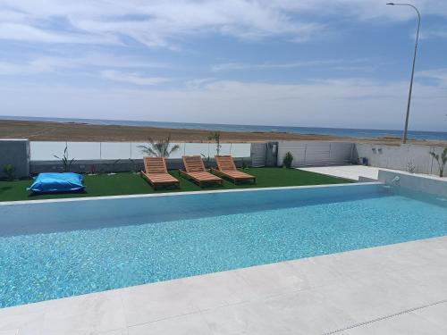 a swimming pool with two chairs and the ocean at Blue Aura Beach villa Larnaca in Pervolia