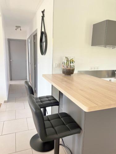 a kitchen with a counter with two black bar stools at Maison Champ du Fort - Jardin & Pétanque à Chablis in Chablis