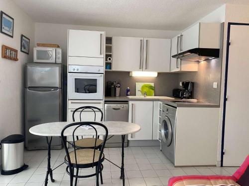 une cuisine avec des armoires blanches et une table et des chaises dans l'établissement Appartement vue mer 3 pièces - Gruissan Ayguades AY110-M04, à Narbonne-Plage