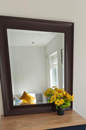 a mirror on a table with a vase of flowers at Entire Cozy home 5 mins from Dublin Airport in Swords