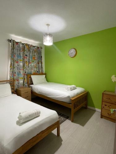 a green room with two beds and a clock on the wall at Chic 2 Bed Apartment with Free Parking- Recently Redecorated, 10 Minutes to City Centre in Edinburgh