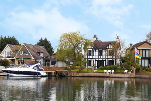 a boat docked at a dock in front of houses at Lux 8Br Thamesfront Villa w Yacht & Sauna in Staines
