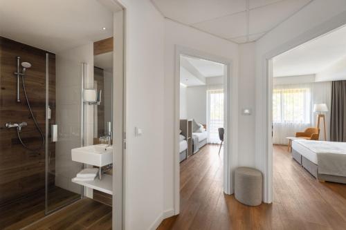 a white bathroom with a sink and a bedroom at Cardoner Hotel és Konferenciaközpont in Dobogoko