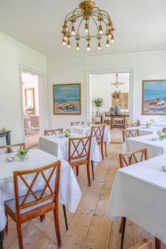 a restaurant with white tables and chairs and a chandelier at Lundsgaard Gods Badehotel in Kerteminde