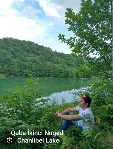a man sitting in the grass next to a lake at Quba A-Frame near Lake & Forest in Quba