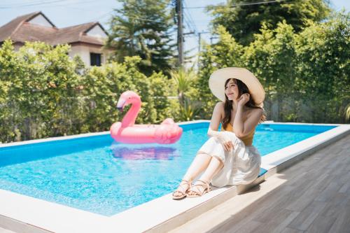 a woman in a hat sitting next to a swimming pool at LakeLyn Pool Villa 5BR , Close to Nimman in Chiang Mai