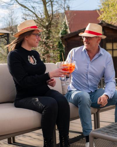 a man and woman sitting on a chair with drinks at Hôtel Restaurant Verger des Châteaux, Route des vins Haut-Koenigsbourg in Dieffenthal