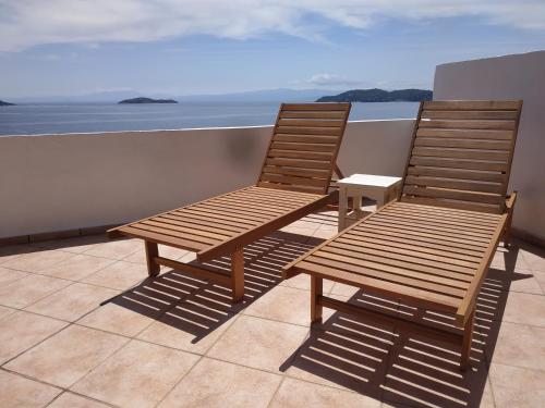 two wooden chairs sitting on a balcony overlooking the ocean at Infinity blue House Skiathos in Skiathos Town