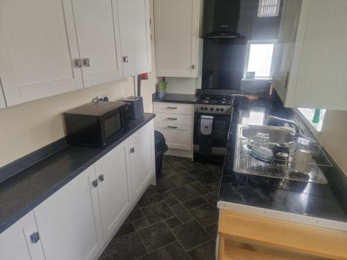 a kitchen with white cabinets and a sink and a microwave at Arundel Road, RM30RX in Harold Wood