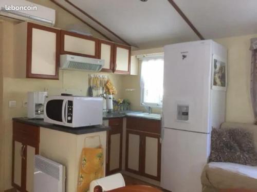 La cuisine est équipée d'un four micro-ondes blanc et d'un réfrigérateur. dans l'établissement Bungalow accueillant avec jardin à Orgnac-l'Aven, à Orgnac-lʼAven