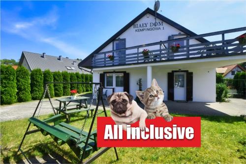 a dog and a cat sitting on a sign in front of a house at Willa Biały Dom - Aquapark Panorama Morska All Inclusive in Jarosławiec
