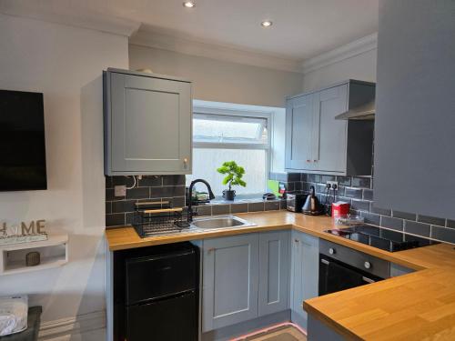 a kitchen with blue cabinets and a sink and a window at Cosy West End Flat Near Leas and Channel tunnel - 8ight Havens Folkestone in Folkestone