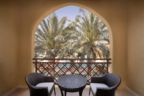 a balcony with a table and chairs and a palm tree at Aldhafra Desert Resort, Vignette Collection by IHG in Madīnat Zāyid