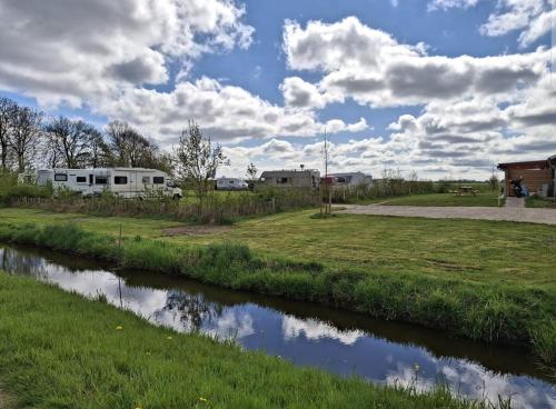 a river in front of a field and a rv at Gezellige caravan met weids uitzicht nabij Sneekermeer in Terzool