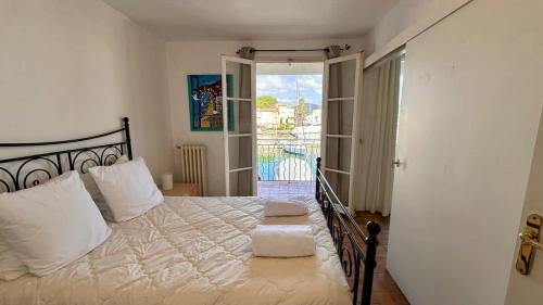 - une chambre avec un lit doté de draps blancs et un balcon dans l'établissement Les Voiliers Appartements vue magnifique, à Grimaud
