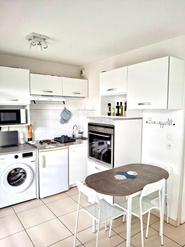 une cuisine avec des armoires blanches et une table et des chaises dans l'établissement Ô Soleil - Spacieux studio entre mer & montagne parking wifi clim, à Saleilles