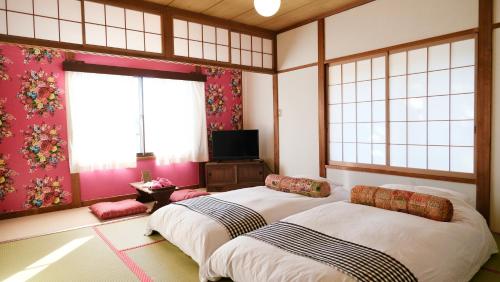 茅野市にあるGuesthouse HOALOHA 4 SEASONSのピンクの壁と窓が特徴の客室で、ベッド2台が備わります。
