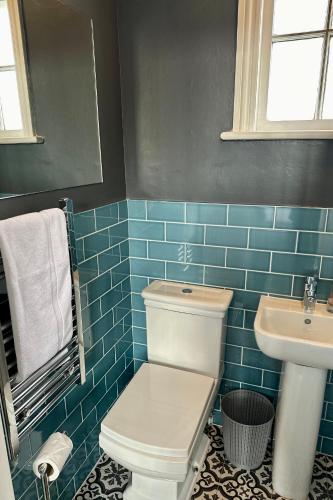 a blue tiled bathroom with a toilet and a sink at The Quarters in Weedon Bec