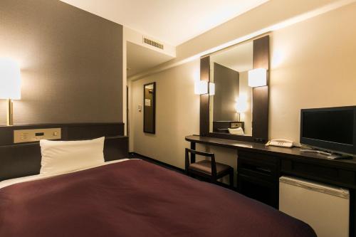 a hotel room with a bed and a desk with a computer at Nishitetsu Inn Kokura in Kitakyushu