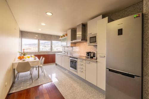 a kitchen with white cabinets and a table and a refrigerator at Panoramic City View Apartment - Guimarães in Guimarães
