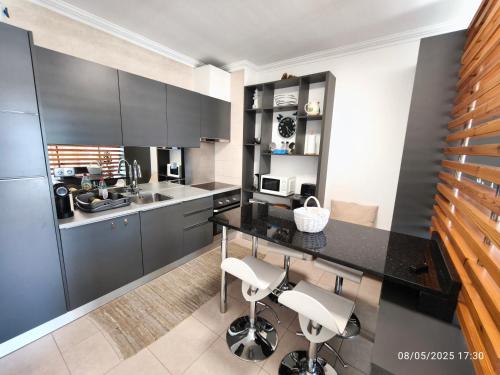 a kitchen with a black counter and white chairs at Apartamento Jeni Residencia Flamingo in Portimão