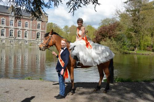 Una mujer con un vestido de novia en un caballo con un hombre en Haras des Chartreux en Estaimbourg