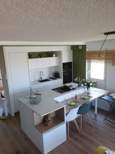 une cuisine avec des comptoirs blancs, une table et des chaises dans l'établissement Les Tamaris Vue Mer, à Roscoff