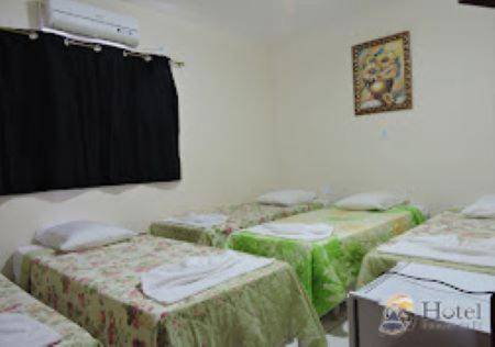 a room with four beds with green linens at Hotel Estação da Fé in Aparecida