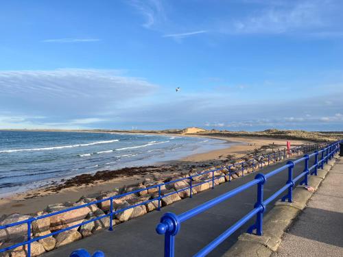 a blue railing next to a beach with the ocean at Sea Breeze St Combs in Fraserburgh
