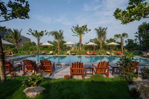 a resort pool with chairs and tables and palm trees at Tam Coc Peaceful Nature in Vũ Lâm