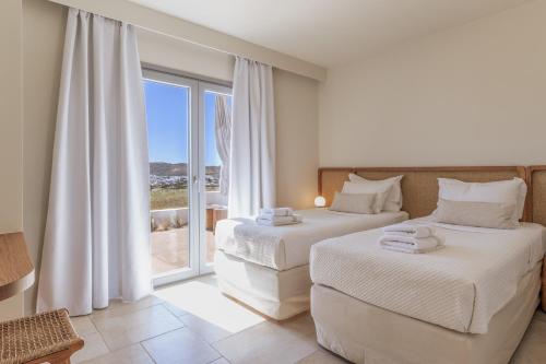 a bedroom with two beds and a large window at Adriana Luxury Villas in Adamas