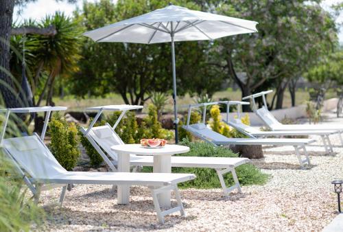 three white chairs and a table and an umbrella at Villa Myricae by Bianco Puglia Vacanze in San Vito dei Normanni