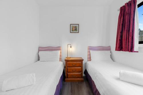 two beds in a room with a nightstand between them at Spacious Wyong Getaway in Wyong