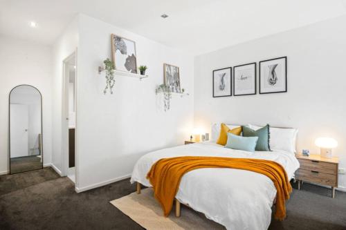 a white bedroom with a bed with an orange blanket at Sunny Richmond Escape 2BR and Large Balcony in Melbourne