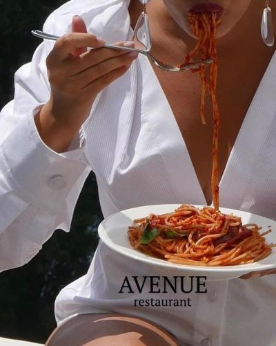 a woman eating a plate of pasta with a fork and knife at Hotel AVENUE in Ravda