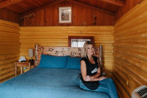 une femme assise sur un lit dans une cabine dans l'établissement Ashton Log Cabins, à Ashton