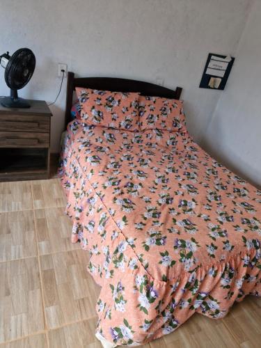 a bed with an orange bedspread with flowers on it at Mini casa interior Teixeira in Augusto de Lima