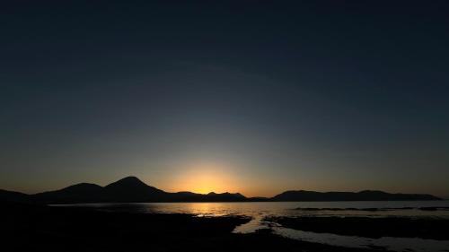 a sunset on the beach with mountains in the background at Carnmhor, Isle of Skye - Stunning 242 year old cottage on its own sea shore! in Breakish