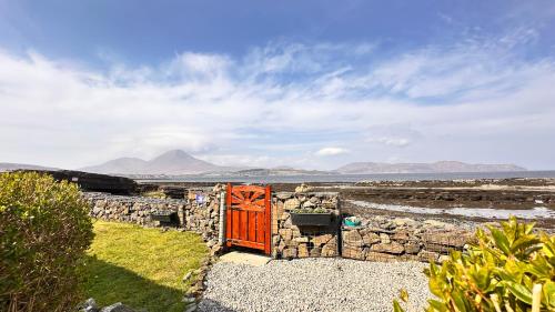 a red door on a stone wall with mountains in the background at Carnmhor, Isle of Skye - Stunning 242 year old cottage on its own sea shore! in Breakish