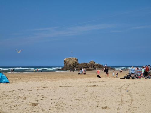 a group of people on a beach with a rock in the ocean at Ocean Breeze-Haven Perran Sands Holiday Park in Perranporth