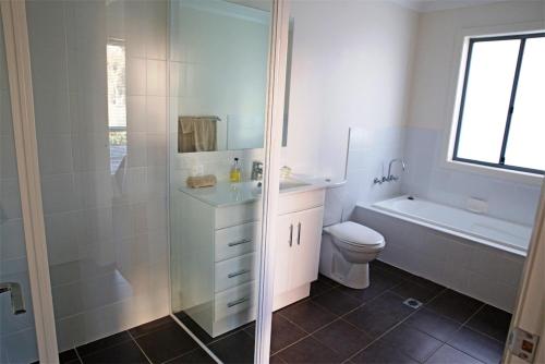a white bathroom with a shower and a toilet at Amooran Oceanside Apartments and Motel in Narooma