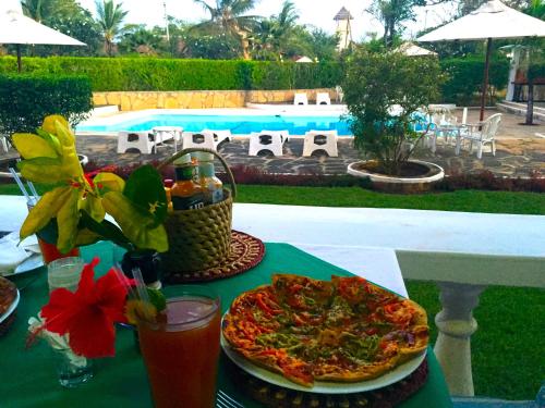 una mesa con una pizza y bebidas y una piscina en Galu Inn en Diani Beach