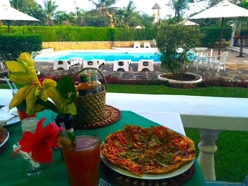 a table with a pizza and drinks and a pool at Galu Inn in Diani Beach