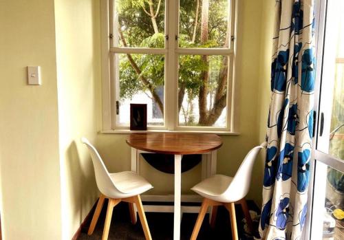 une table et deux chaises devant une fenêtre dans l'établissement Paekākāriki Cottage near the Sea, à Paekakariki