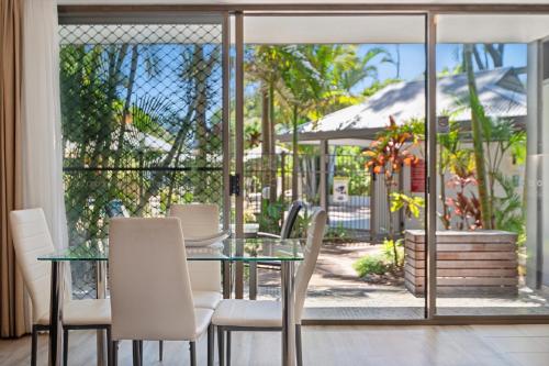 a dining room with a glass table and white chairs at Smugglers On The Beach in Coffs Harbour