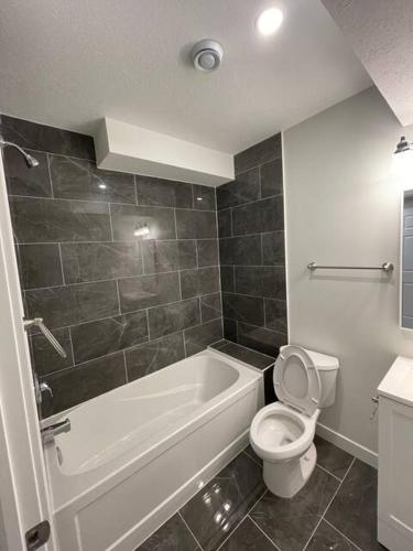 a bathroom with a white tub and a toilet and a sink at Bedroom in Southwest D in Edmonton