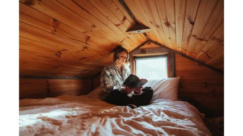 a woman sitting on a bed reading a book at Little Blue Wren by Tiny Away in Yea