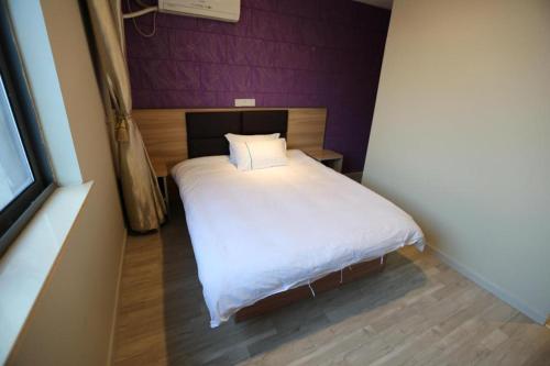 a small bedroom with a white bed and a purple wall at Shanghai Jiejia hotel in Shanghai