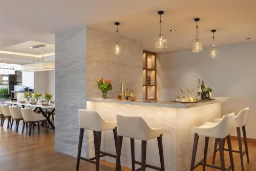 a kitchen and dining room with a bar with white stools at Siam Kempinski Hotel Bangkok in Bangkok