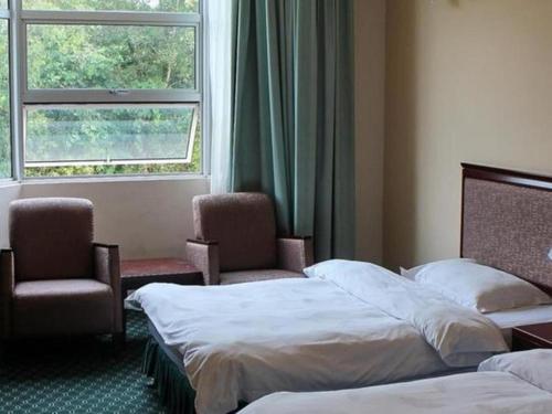 a hotel room with two beds and chairs and a window at Traders Inn Brunei in Bandar Seri Begawan